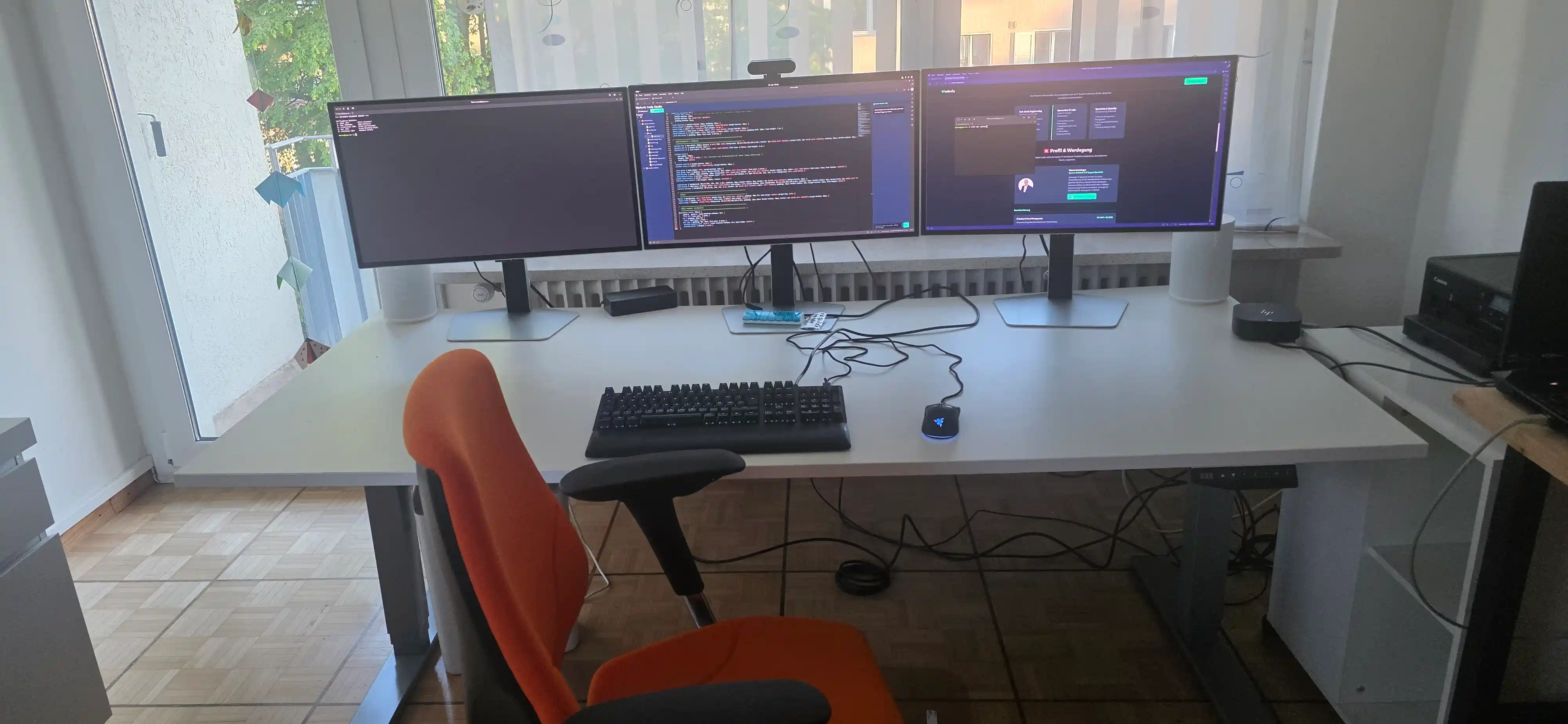Professioneller IT-Arbeitsplatz von Marco Henninger mit einem ergonomischen Triple-Monitor-Setup zur Systemüberwachung und Code-Entwicklung